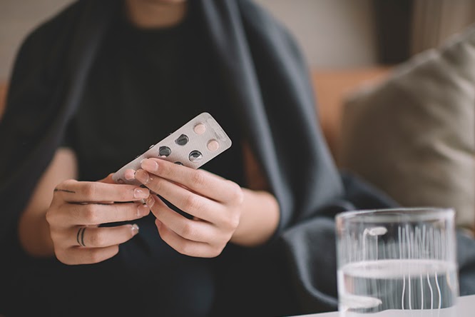 Young woman takes medication out of blister pack.